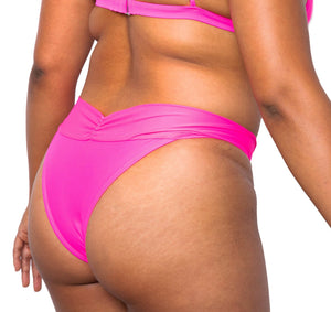 Model looking back wearing MIGA Ally Bikini Bottom with Crossover Waistband in Neon Pink. Wearing matching MIGA Ally Bikini Top.