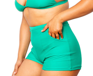 Model with hand in pocket wearing MIGA Ally Boy Shorts in Emerald Green with matching MIGA Ally Bikini Top.