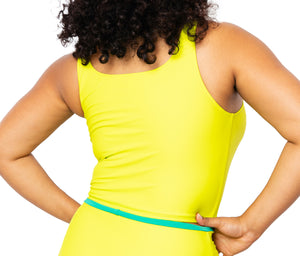
            
                Load image into Gallery viewer, Model facing back wearing lime green tankini top with scoop neck that comes with a front pocket with emerald green detail. She is also wearing matching lime green high-waisted bikini bottom with moderate coverage.
            
        