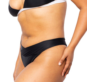 Model wearing MIGA Ally Bikini Bottom with Crossover Waistband in Black. Wearing matching MIGA Ally Bikini Top in Black and White.