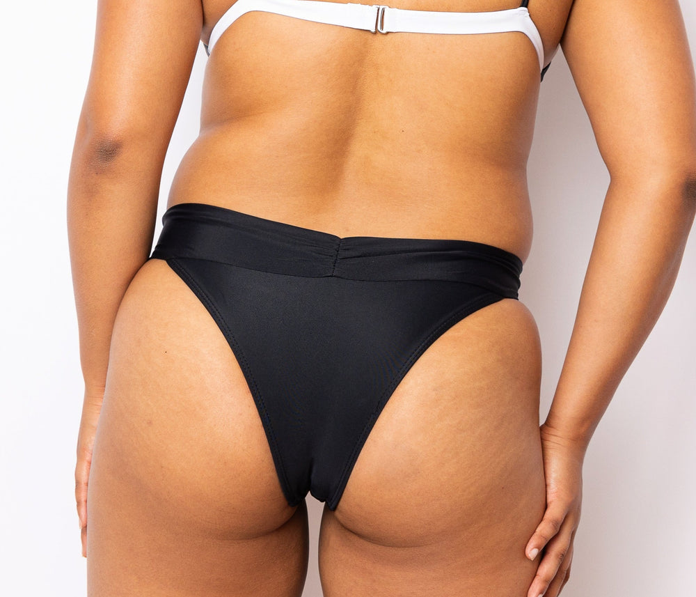 
            
                Load image into Gallery viewer, Model looking back wearing MIGA Ally Bikini Bottom with Crossover Waistband in Black. Wearing matching MIGA Ally Bikini Top in Black and White.
            
        
