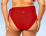 Closeup of model showing her stoma bag in torso, wearing burnt orange high-waisted bikini bottom with unsnapped belt and burnt orange long sleeves top.