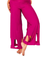 Model showcasing arc cutouts of magenta high waisted pants. Feet in sand.